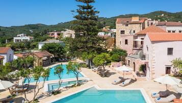 Un resort con piscina central, sillas de descanso y montañas al fondo.
