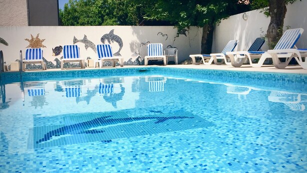 A swimming pool with blue mosaic tiles, white lounge chairs, and decorative wall art. - Motel Capsol (Mandelieu-La-Napoule)