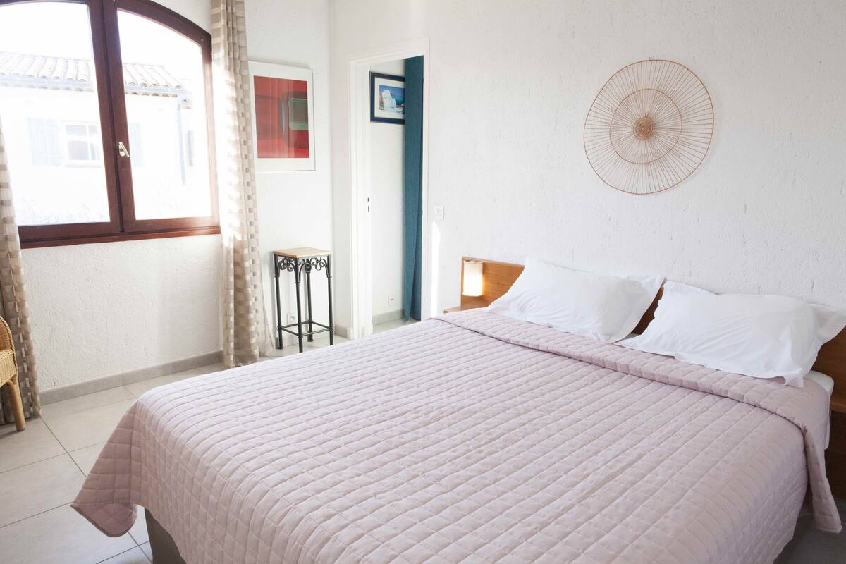 Une chambre avec un grand lit, un ventilateur fixé au mur et une fenêtre avec des rideaux.