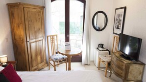 A hotel room with a bed, a wooden wardrobe, a television, a small table with a chair, and a balcony with a view. - Motel Capsol (Mandelieu-La-Napoule)