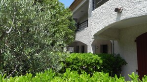 A building with a white stucco exterior, balconies, and a garden with various plants. - Motel Capsol (Mandelieu-La-Napoule)