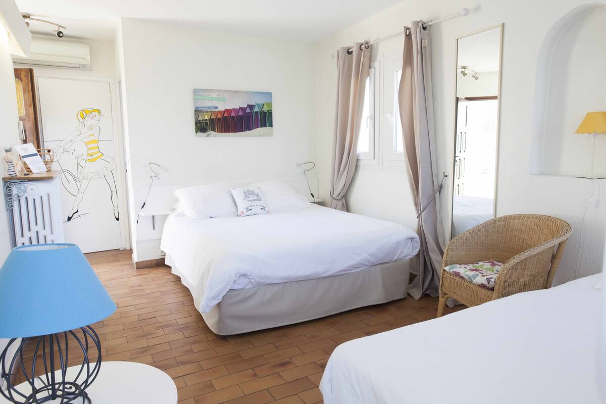 Une chambre d’hôtel avec un lit, une chaise en osier, un bureau avec une lampe et un tableau au mur.