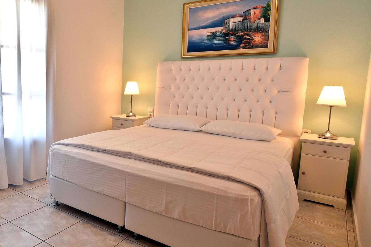 Un dormitorio ordenado con una cama grande, dos mesitas de noche con lámparas y un cuadro en la pared.