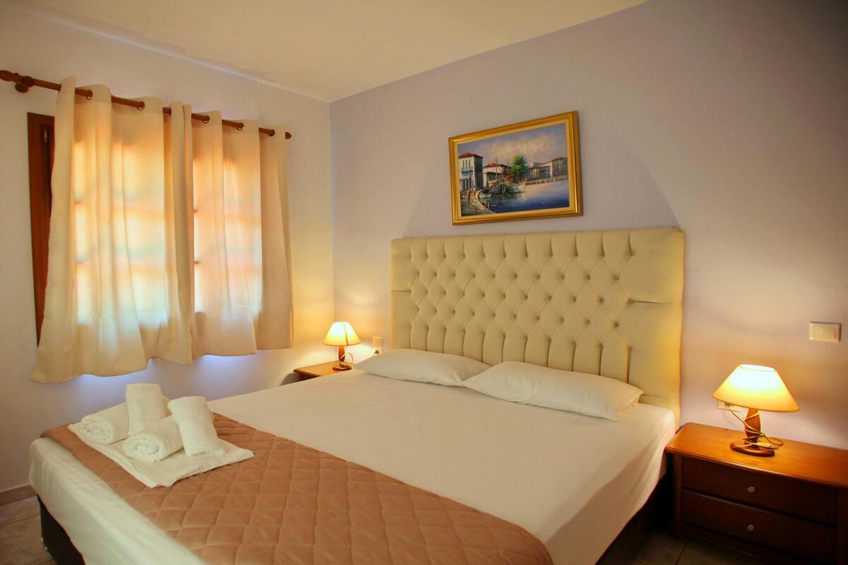 Una habitación de hotel con una cama grande, dos lámparas de noche, un cuadro en la pared y una ventana con cortinas.