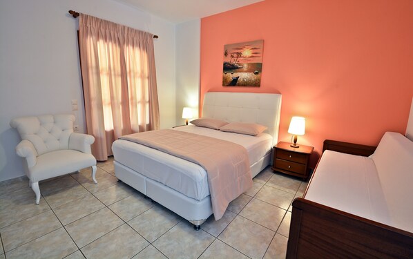 A bedroom with a bed, two bedside tables, a chair, and a painting on the wall. - Anna Maria – Vanessa Apartments (Skopelos)