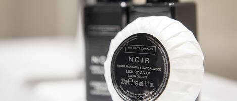 A bottle of Noir luxury soap with a black label and white cap, placed in front of a black box.