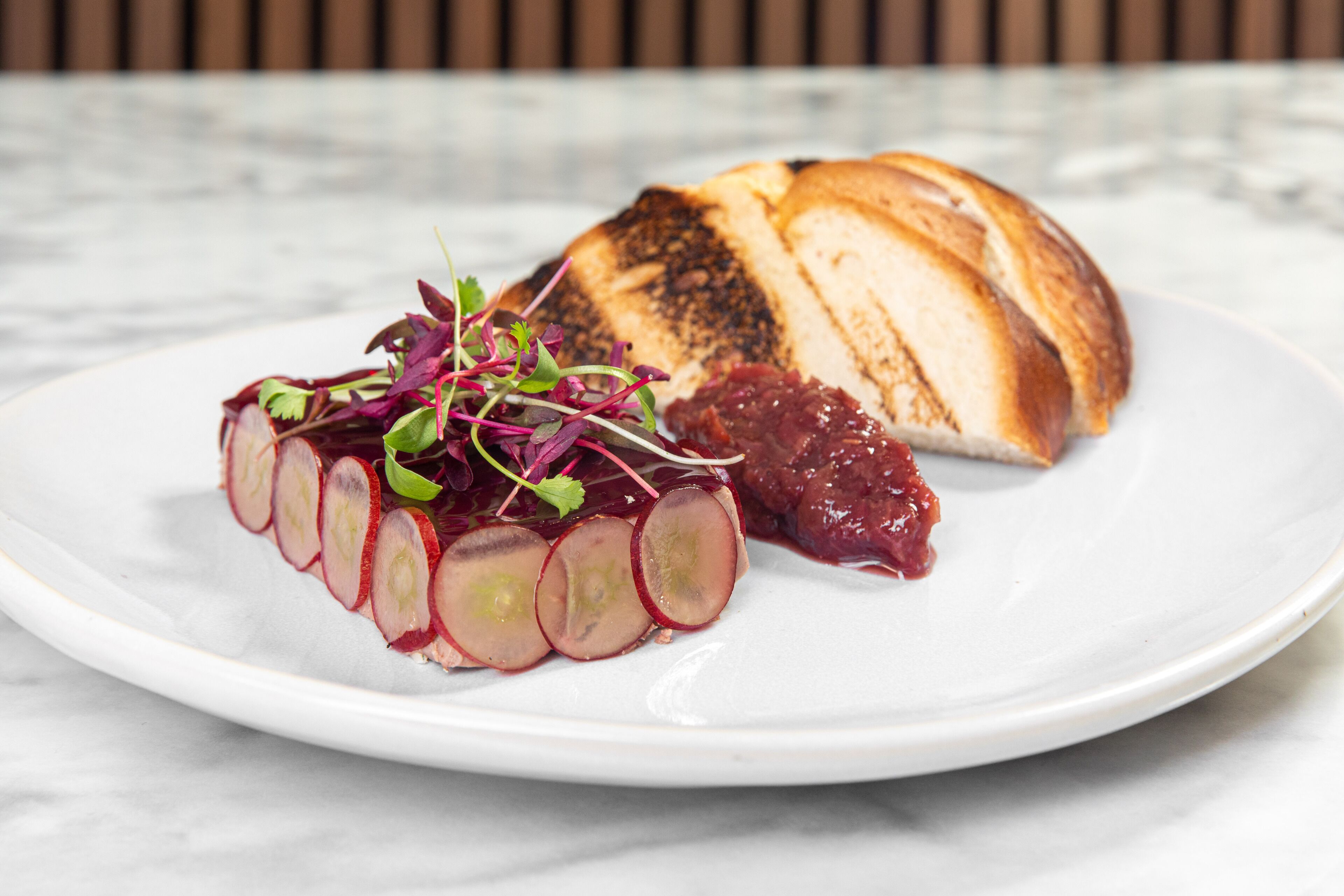A white plate with sliced radishes, a piece of grilled bread, and a small amount of red sauce.