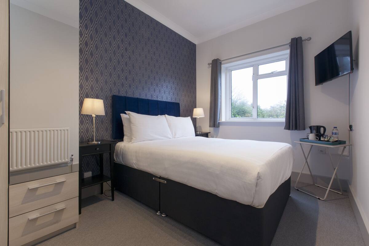 A hotel room with a bed, bedside tables, a TV, and a window with curtains.