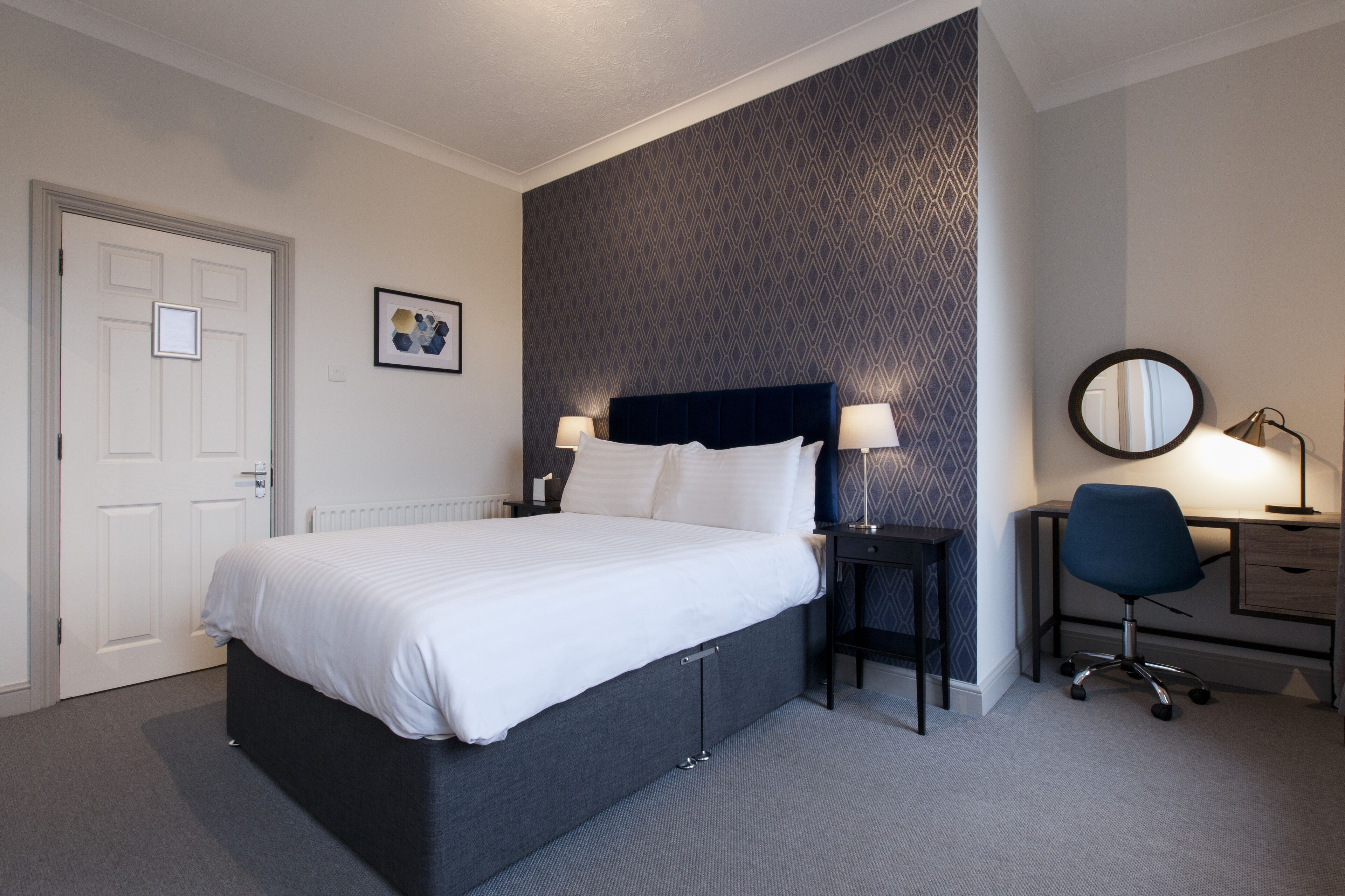 Una habitación de hotel ordenada con una cama grande, mesitas de noche, un escritorio y una silla.