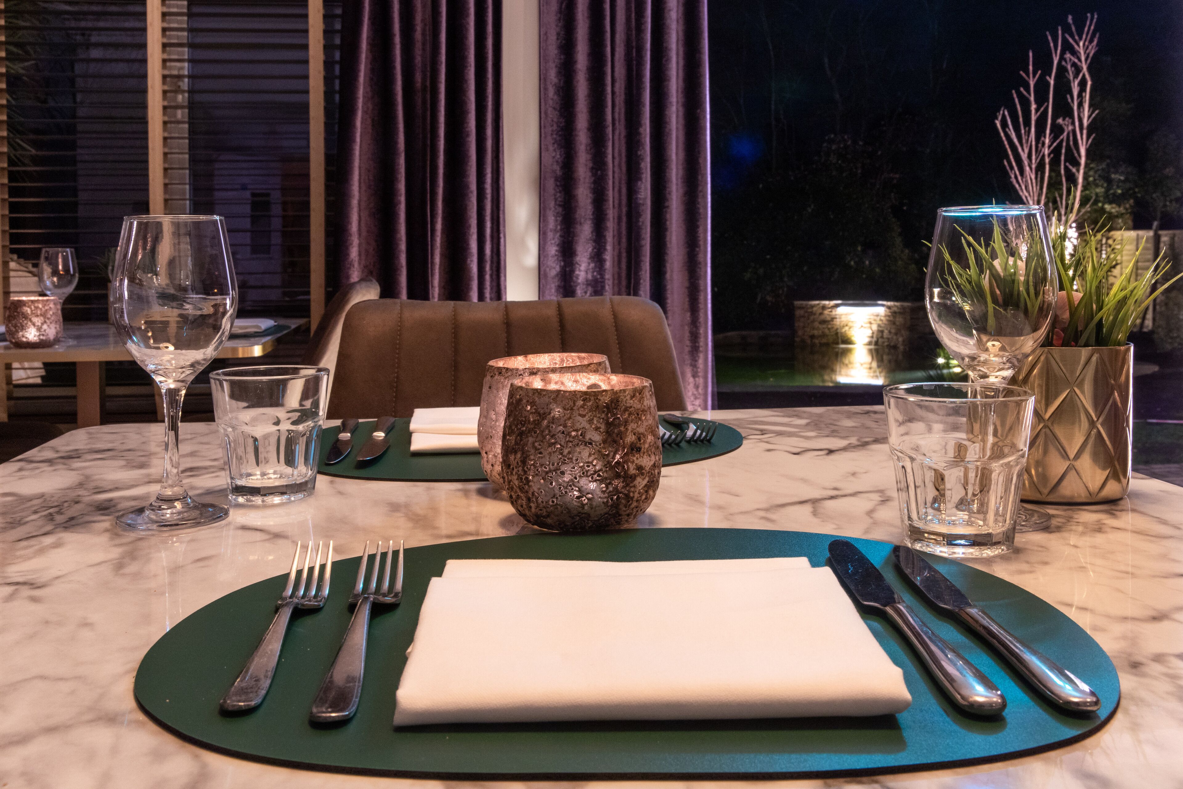 A table set for dining with a green placemat, white napkin, cutlery, and clear glasses.