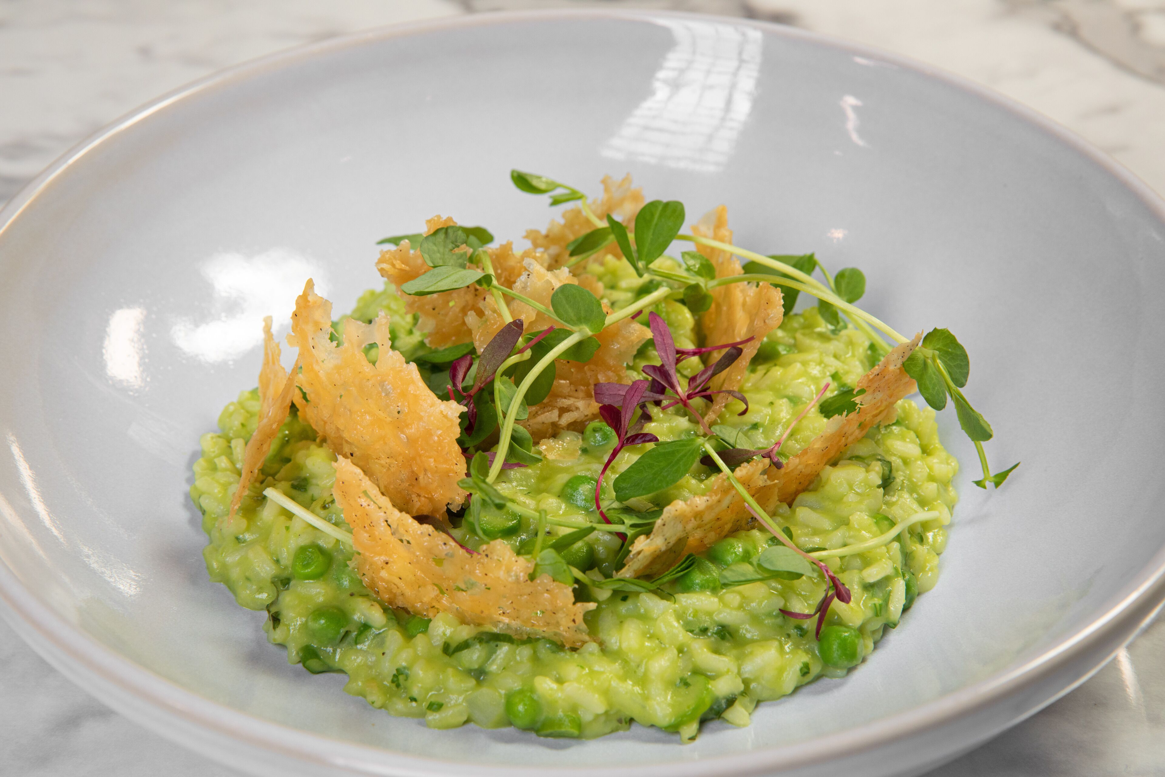 Une assiette de risotto vert, agrémentée de jeunes pousses et d’éléments croustillants.