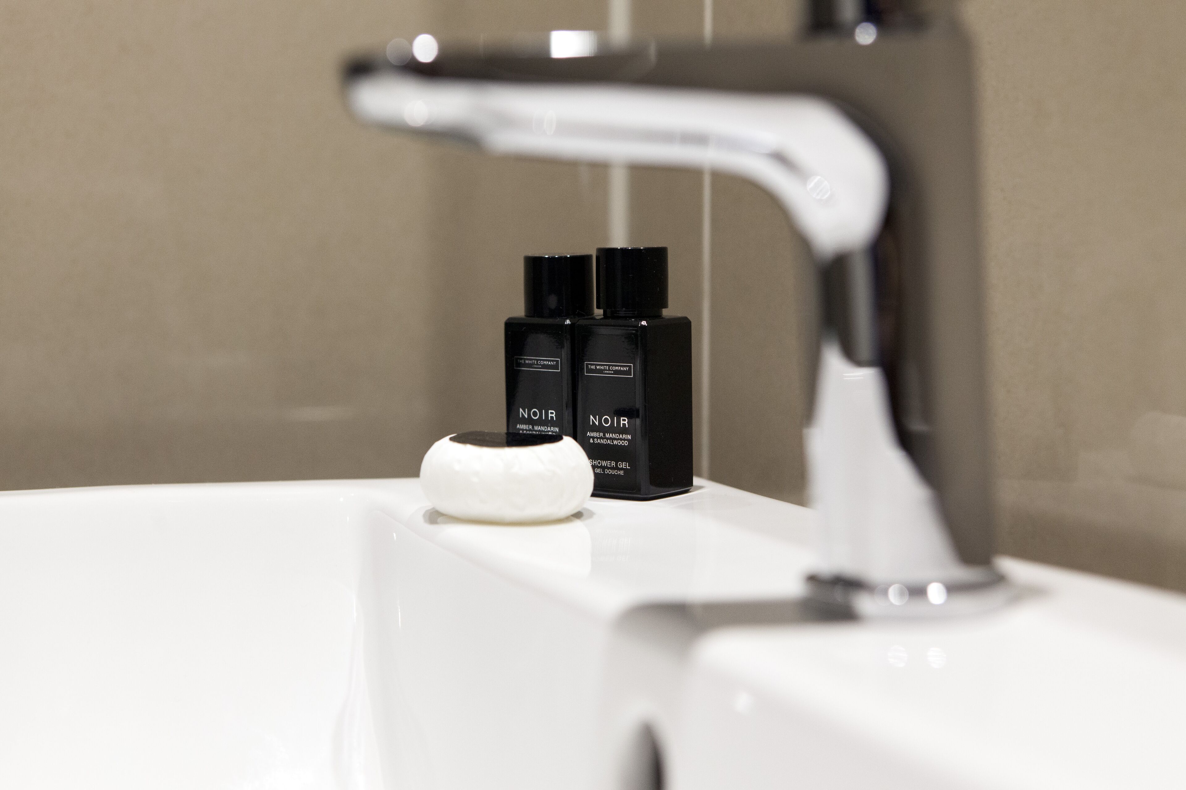 Uma pia de banheiro com uma torneira moderna e duas garrafas pretas com a etiqueta "NOIR" sobre o balcão.
