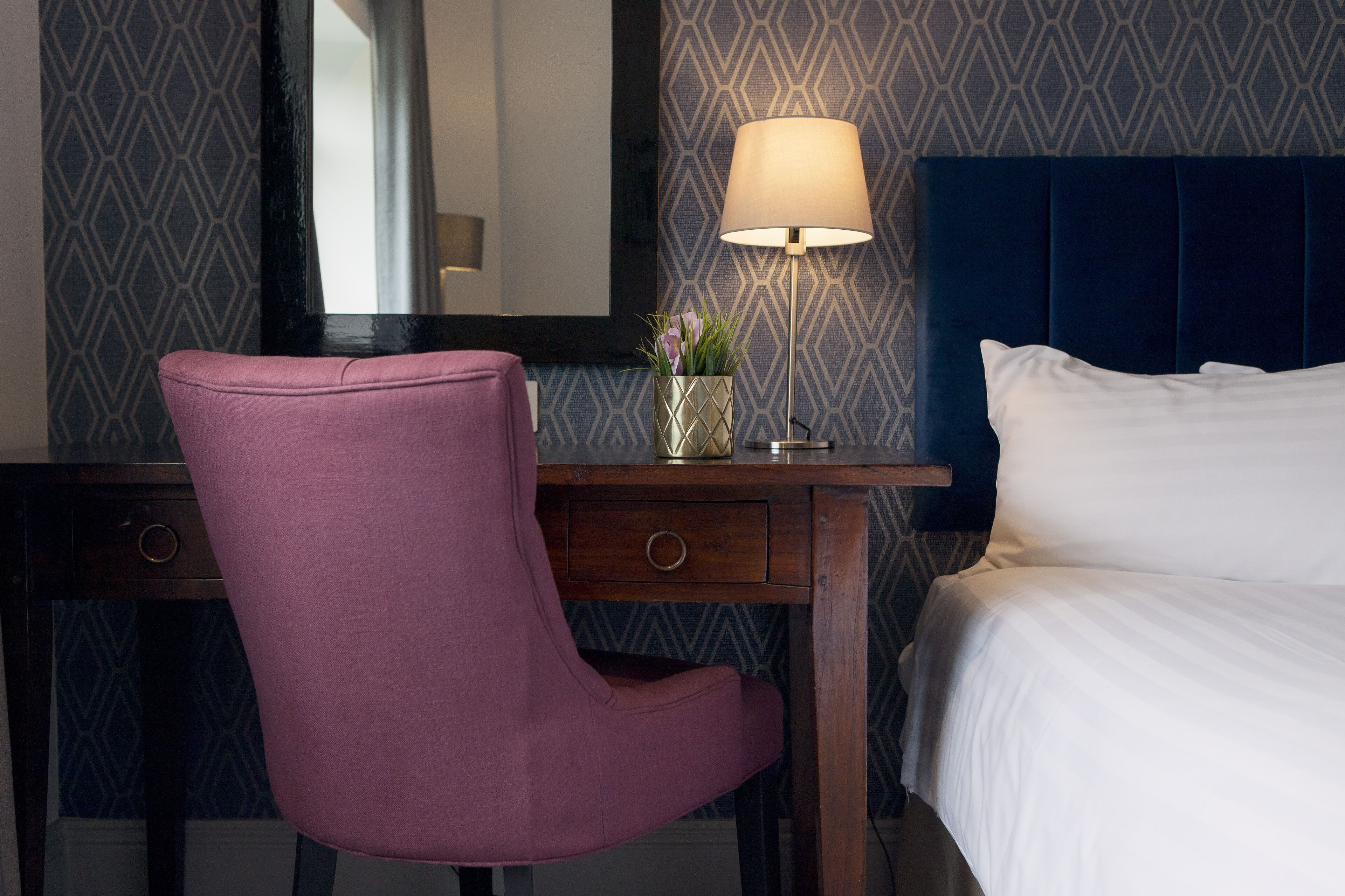 Une chambre d’hôtel comprenant un lit, un bureau avec une lampe, une chaise et une plante décorative.