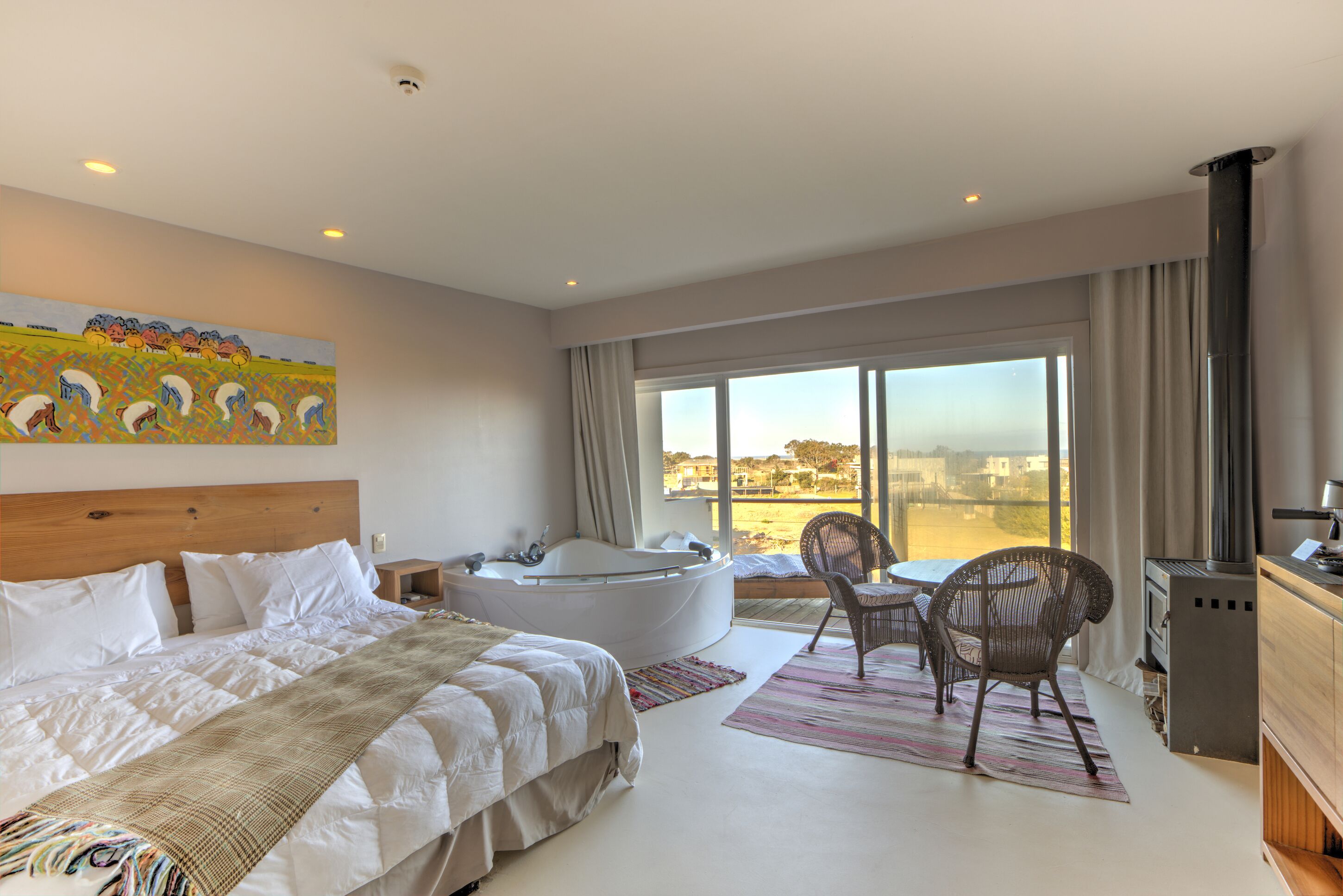 Quarto de hotel moderno com uma cama grande, banheira, área de refeições com cadeiras e vista para a cidade.