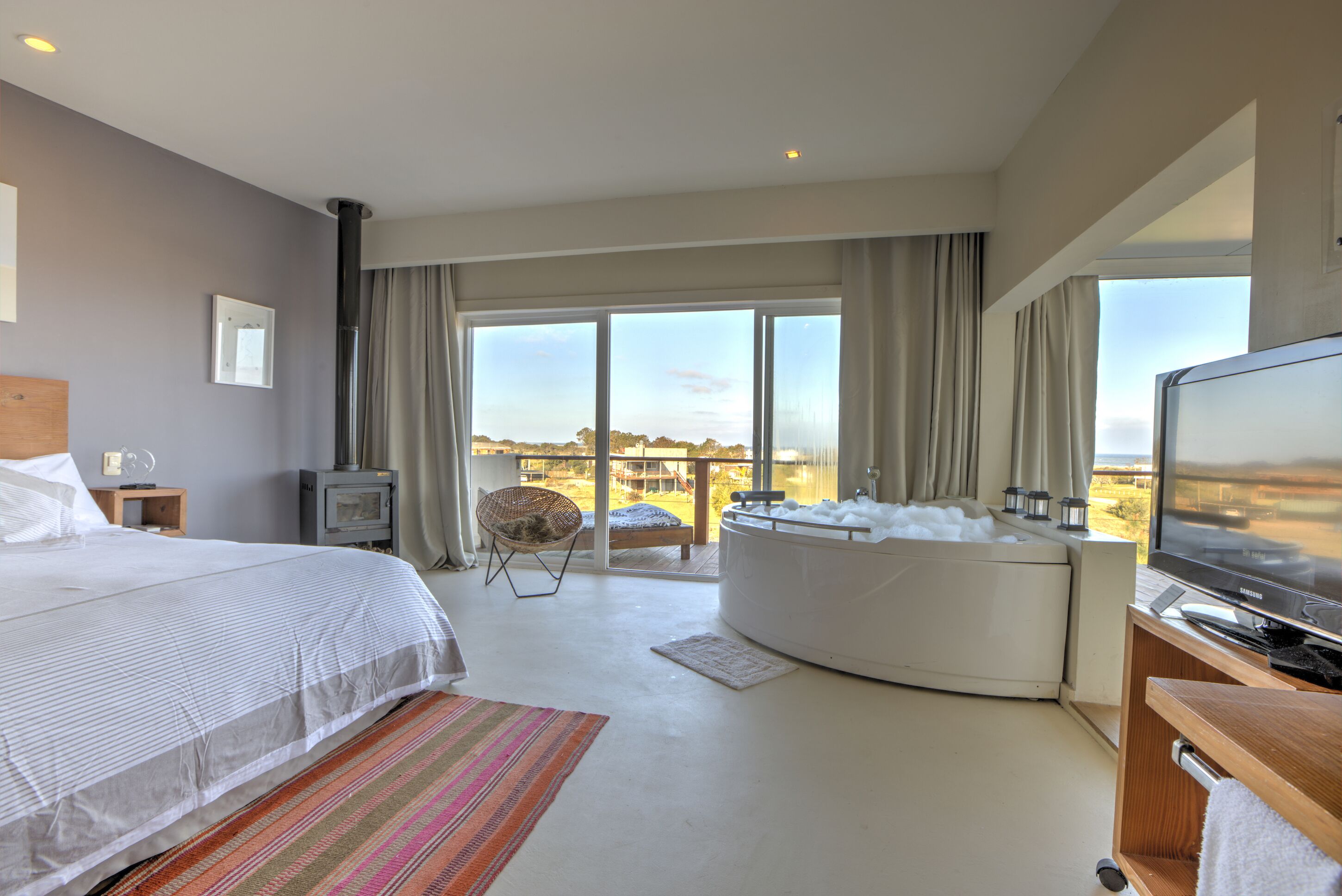 A hotel room with a bed, a TV, a hot tub, and a view of the outdoors.