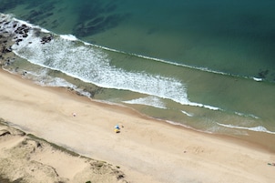 Vista aérea de una playa con aguas cristalinas, orilla arenosa y algunas personas.