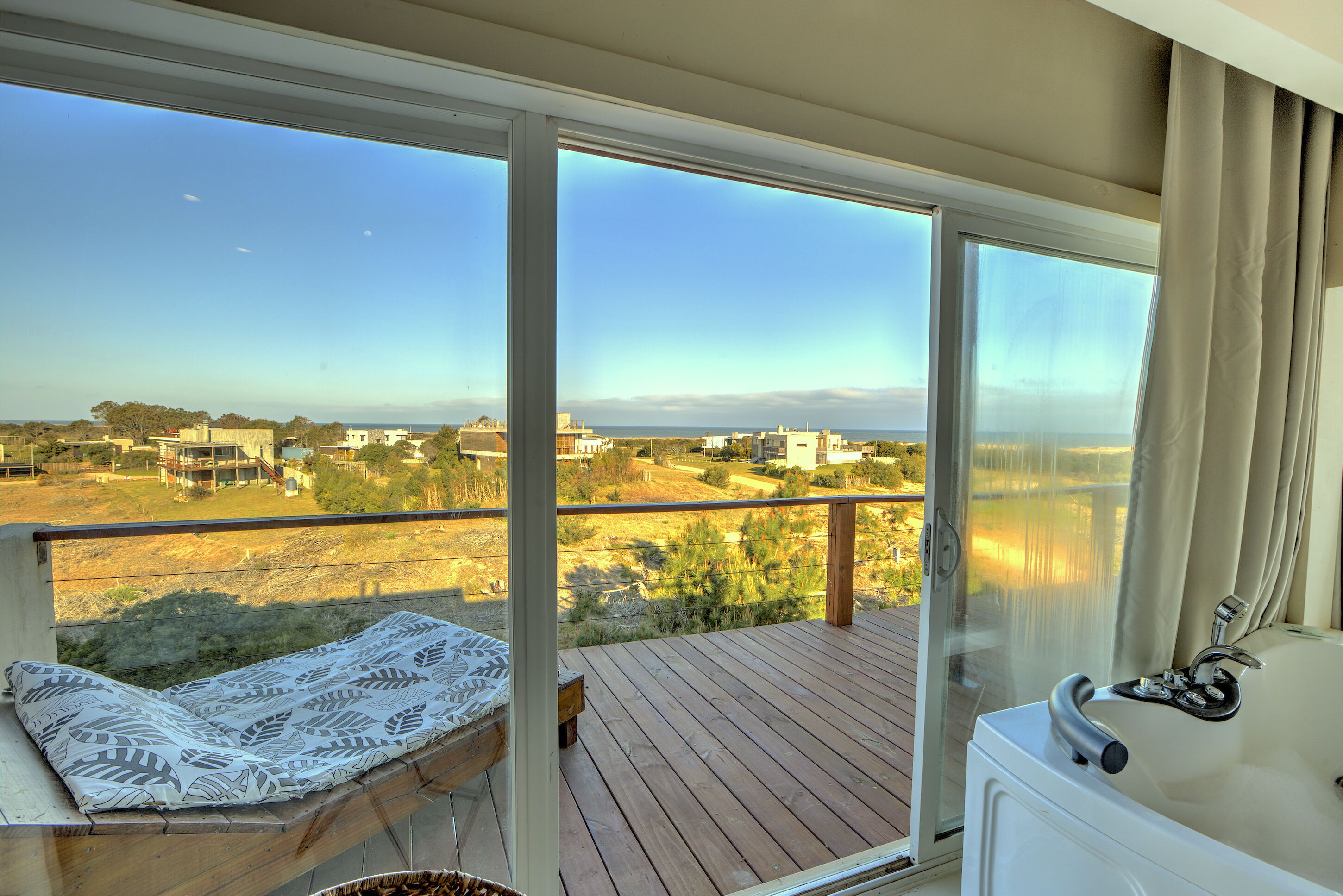 A balcony with a wooden deck, a cushioned seating area, and a view of a distant landscape.