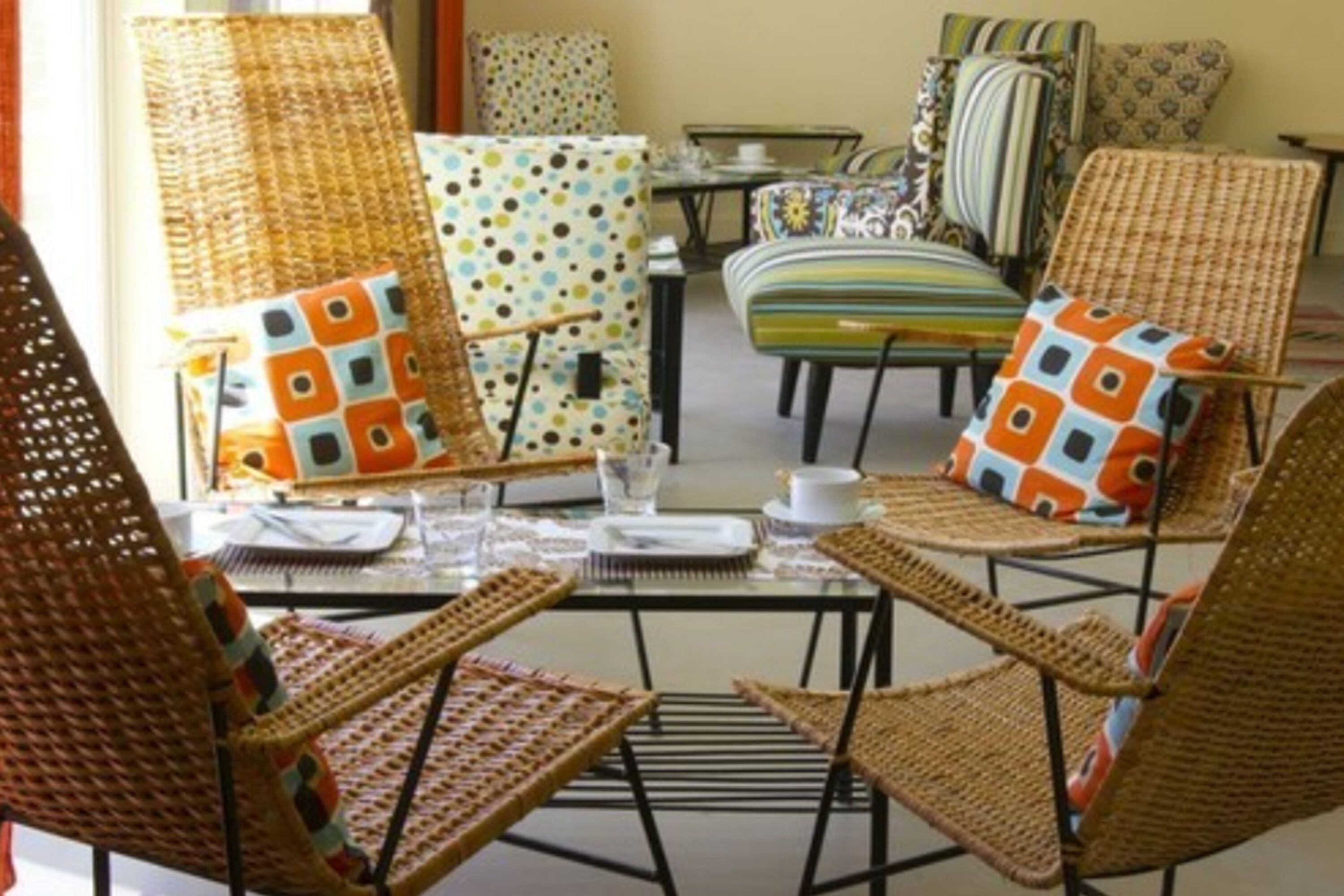 A room with wicker chairs and tables, some with colorful cushions.