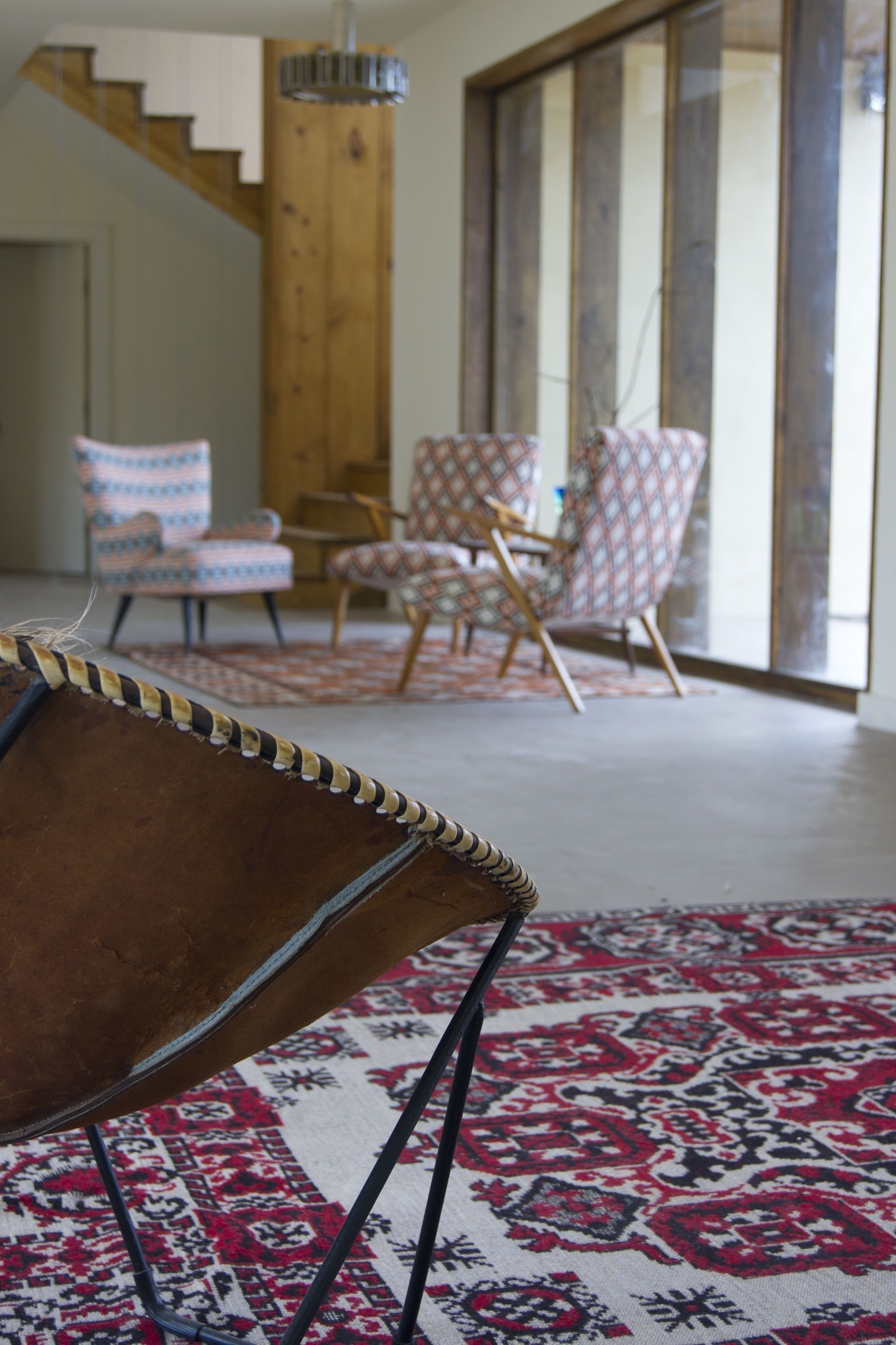 A modern living room with a patterned rug, a brown leather chair, and patterned chairs.