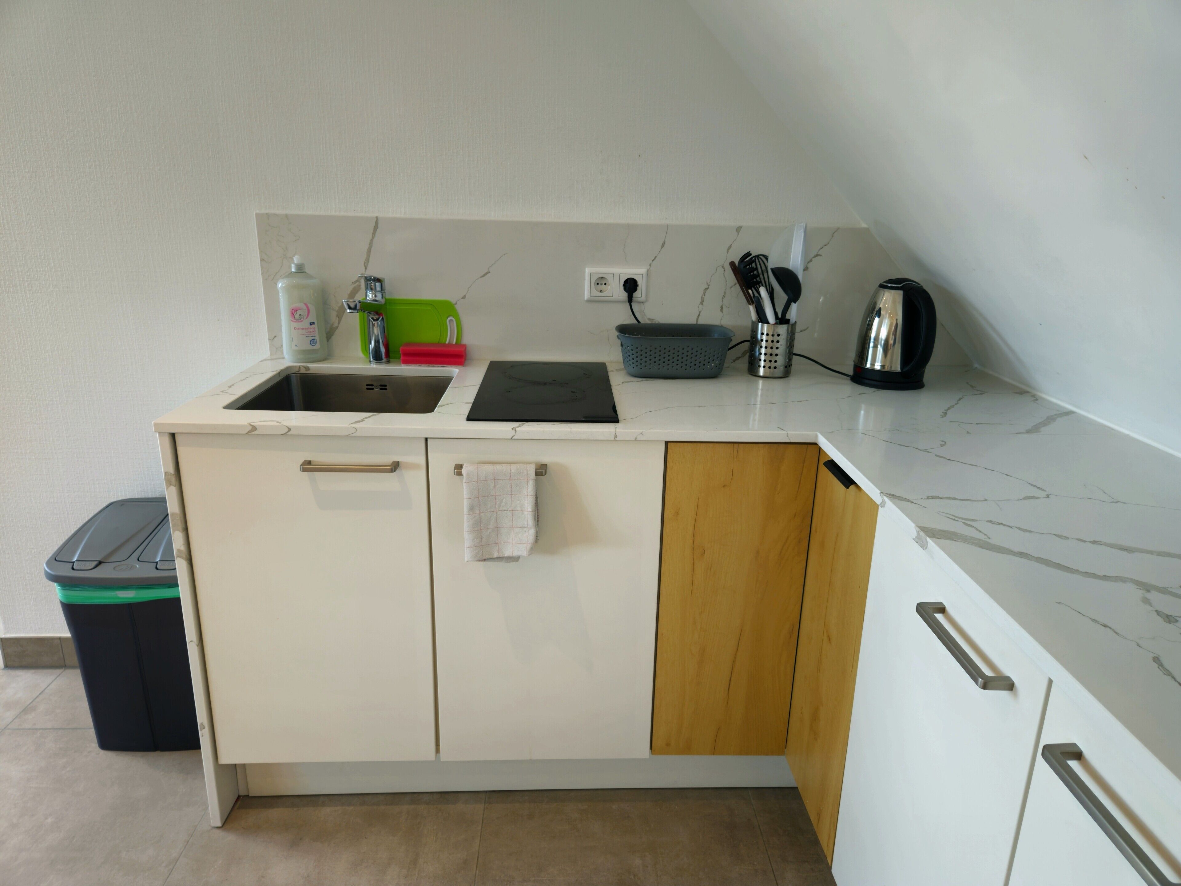 Eine kleine Küche mit Spüle, Wasserkocher und Sieb auf der Arbeitsplatte.
