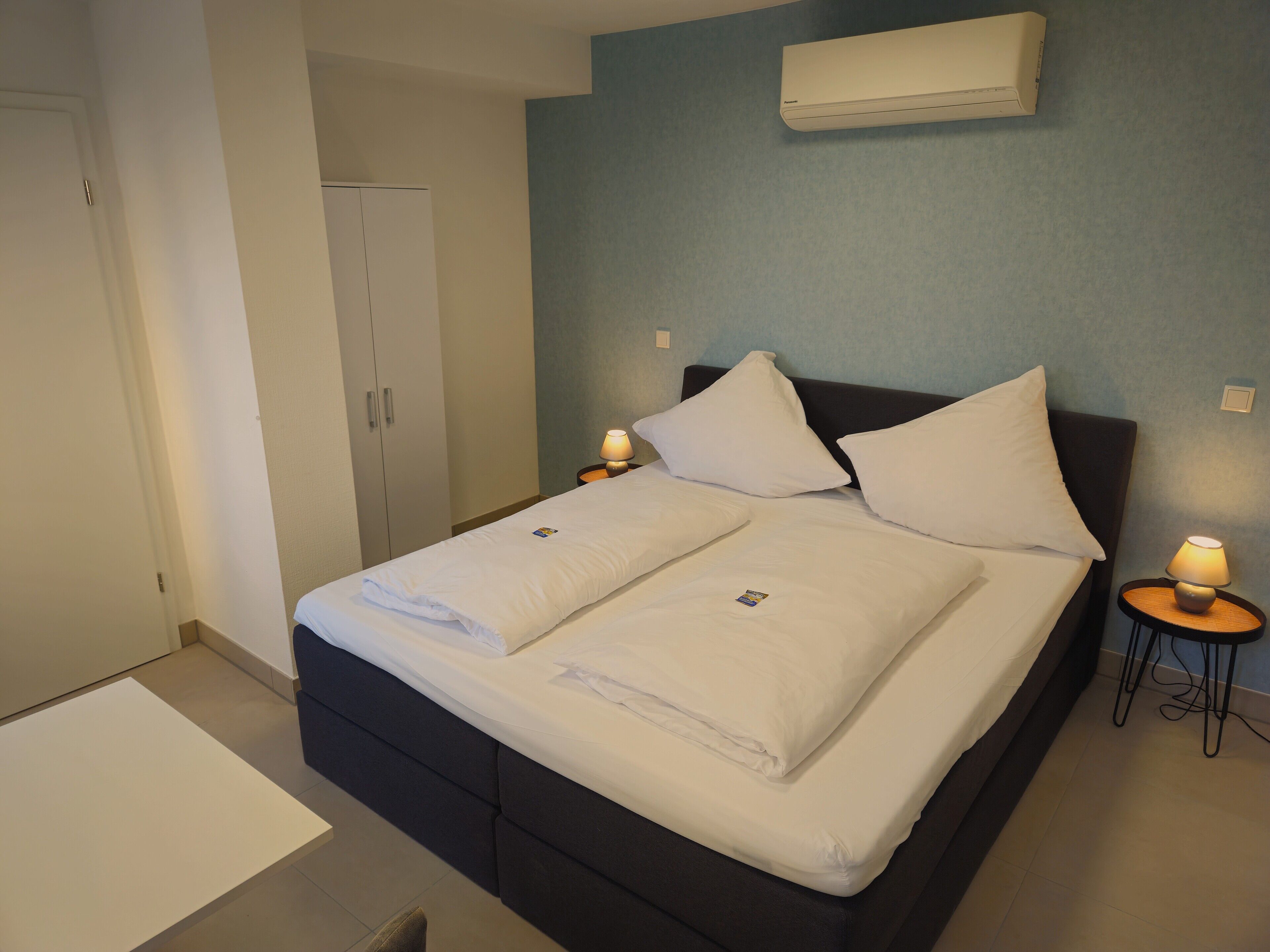 A neatly made bed with white linens, a dark headboard, and two bedside lamps.