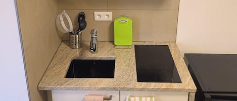 A kitchen with a double sink, a stove, and a small trash bin.