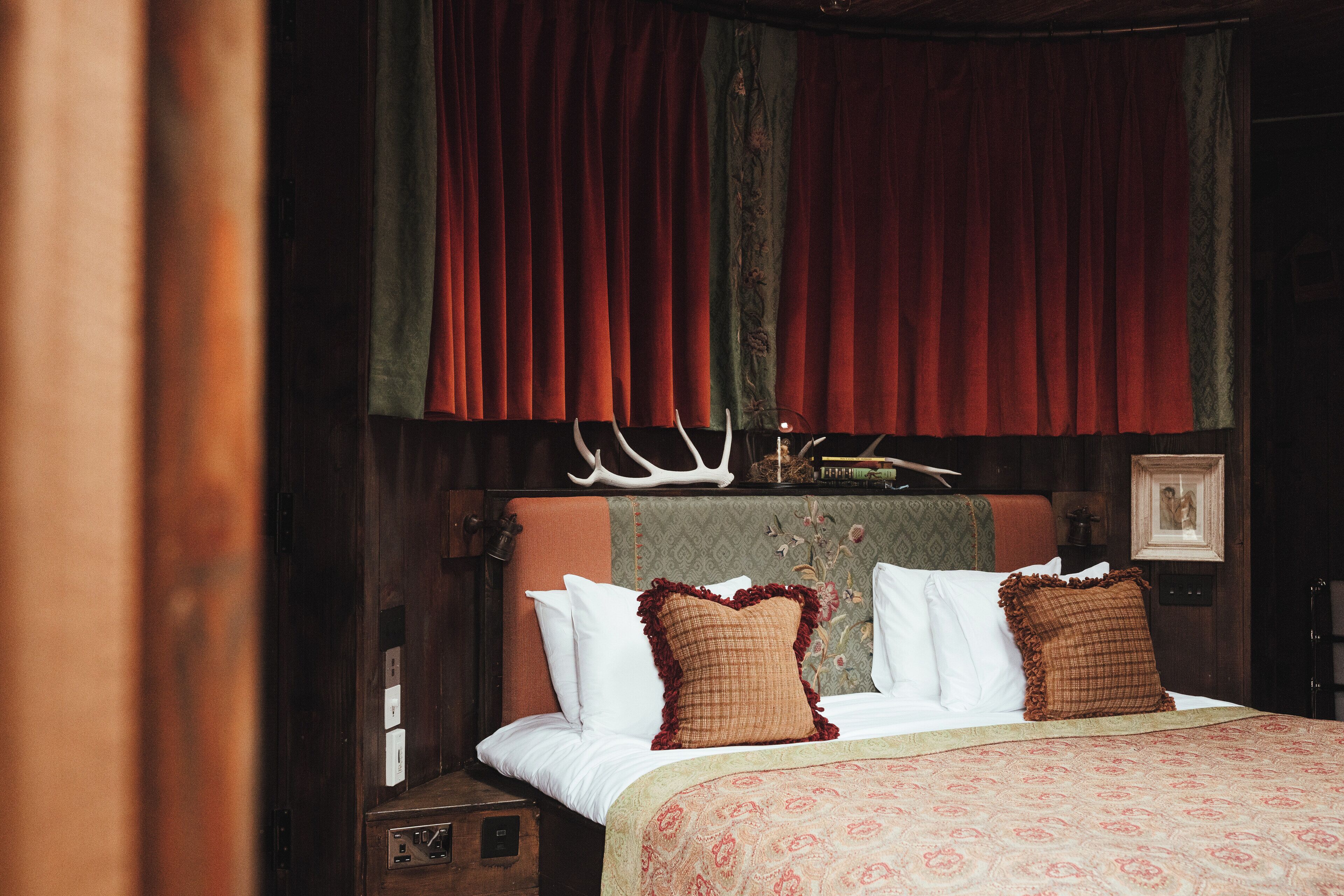 A bedroom with a bed, curtains, a headboard with antlers, and a framed picture on the wall.