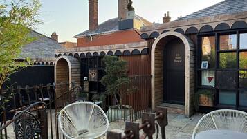 Un patio con sillas de mimbre y una mesa, un edificio con un cartel que dice "The Bird House", y chimeneas de ladrillo.