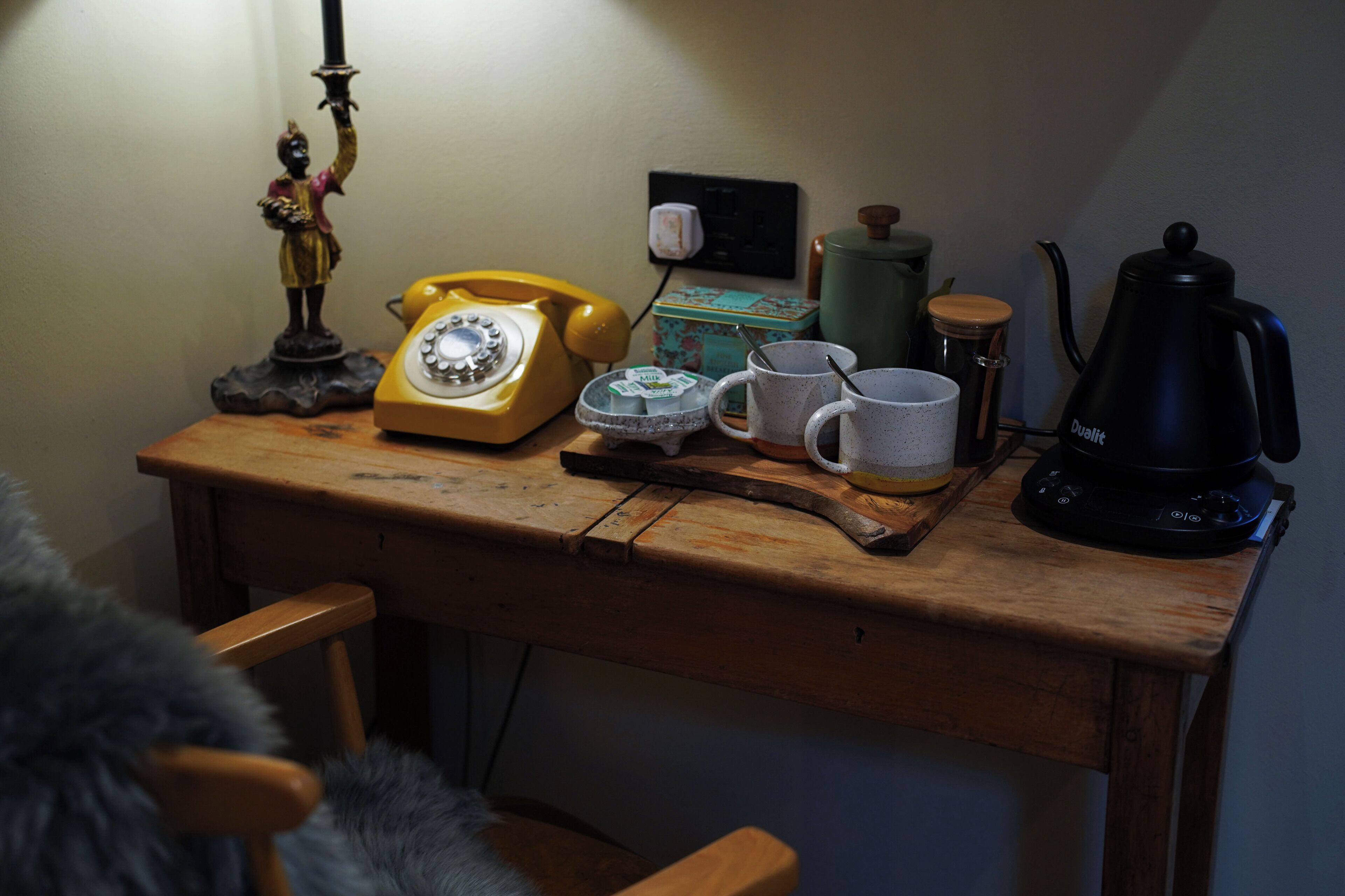 Een houten bureau met een vintage gele telefoon, een groene waterkoker, een witte mok en een zwarte koffiepot.