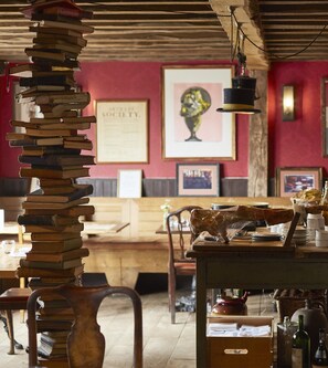 A cozy restaurant interior with a stack of books, wooden furniture, and framed artwork on the walls.