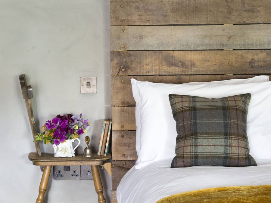 A bedroom with a wooden headboard, a bed with a yellow blanket, a nightstand with a vase of flowers, and a lamp.