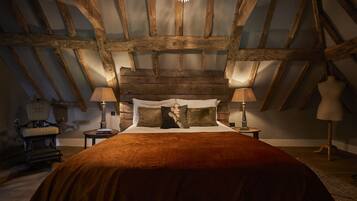 A bedroom with a wooden ceiling, a bed with a brown blanket, two bedside lamps, and a chair with a cushion.