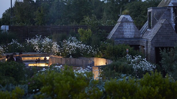 A rustic building with a sloped roof and a small window, surrounded by lush greenery and white flowers. - The Bell in Ticehurst (Wadhurst)