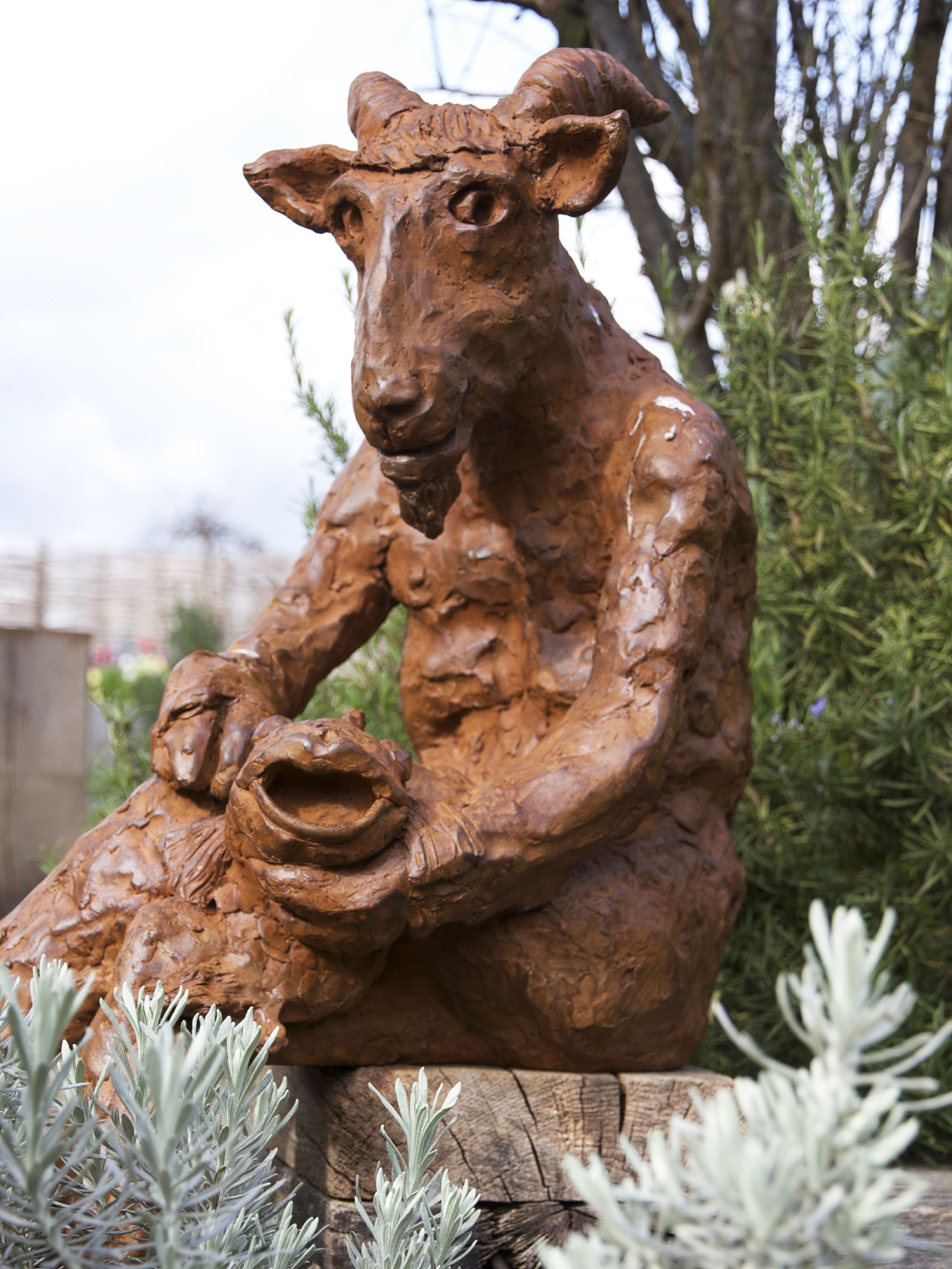 A sculpture of a seated figure with a child, surrounded by greenery.