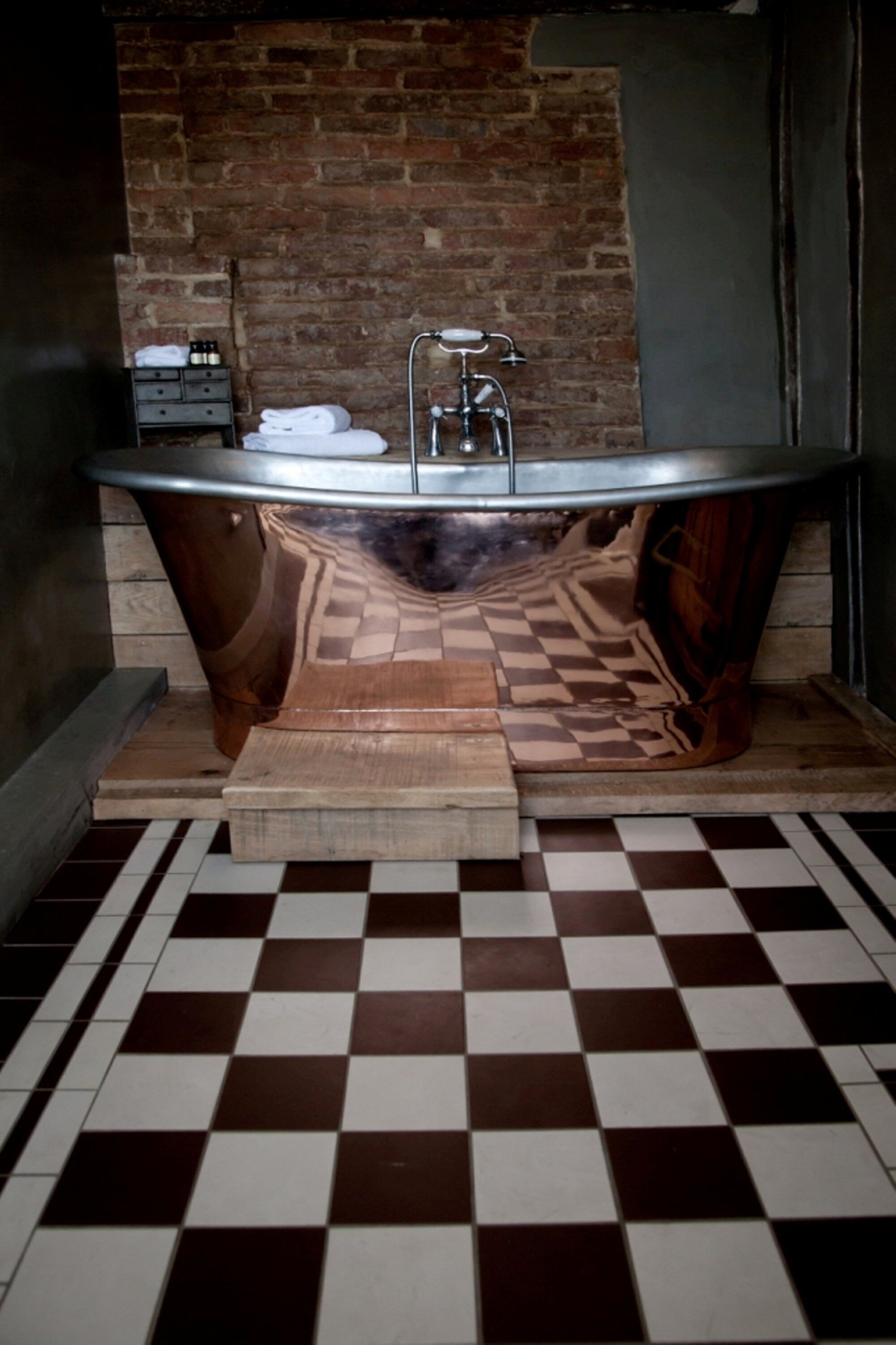 Un baño con piso a cuadros, tocador de madera y pared de ladrillo.