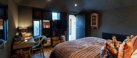 A bedroom with a large bed, a desk, and a chair. There is a window and a door leading to another room.