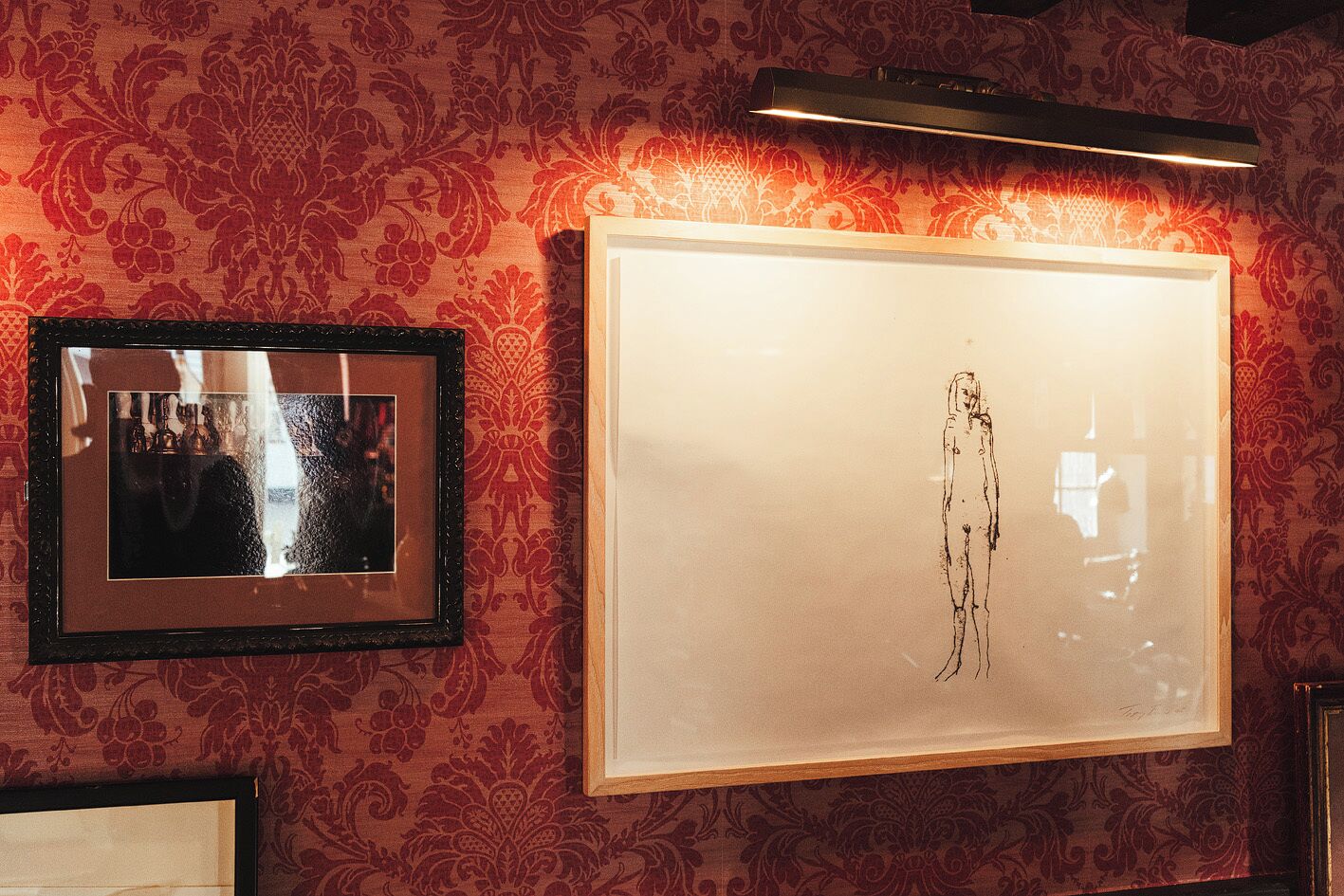 A wall with two framed artworks, one depicting a figure and the other showing a group of people.