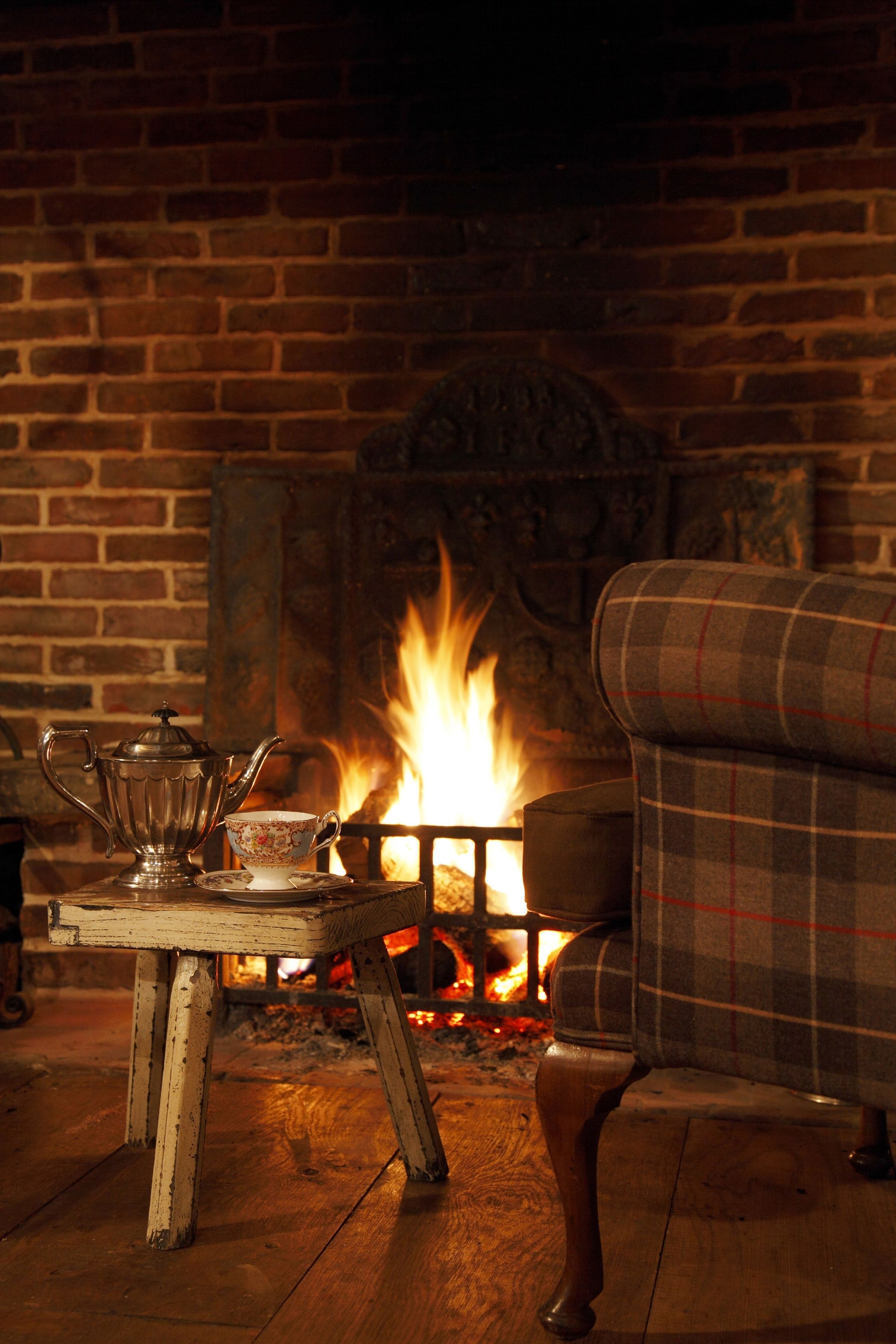 A cozy room with a brick fireplace, a plaid armchair, and a table with a silver teapot and cup.