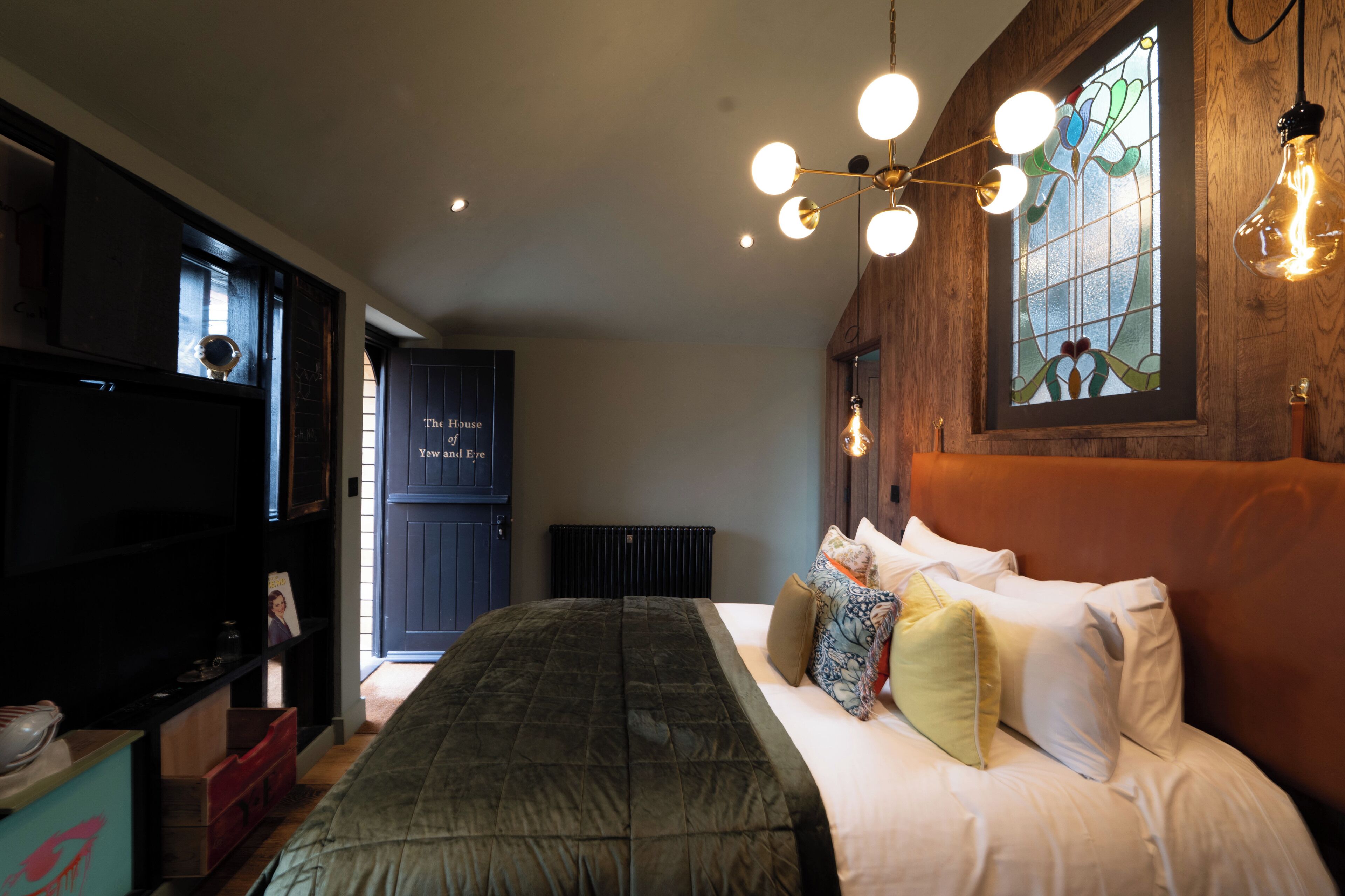 A bedroom with a bed, a wooden headboard, a stained glass window, and a ceiling light fixture.