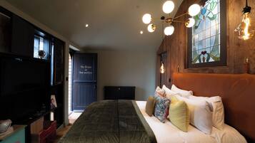 A bedroom with a bed, a wooden headboard, a stained glass window, and a ceiling light fixture.