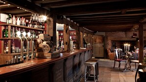 A bar area with wooden beams, shelves of liquor bottles, and a bar counter with stools. - The Bell in Ticehurst (Wadhurst)