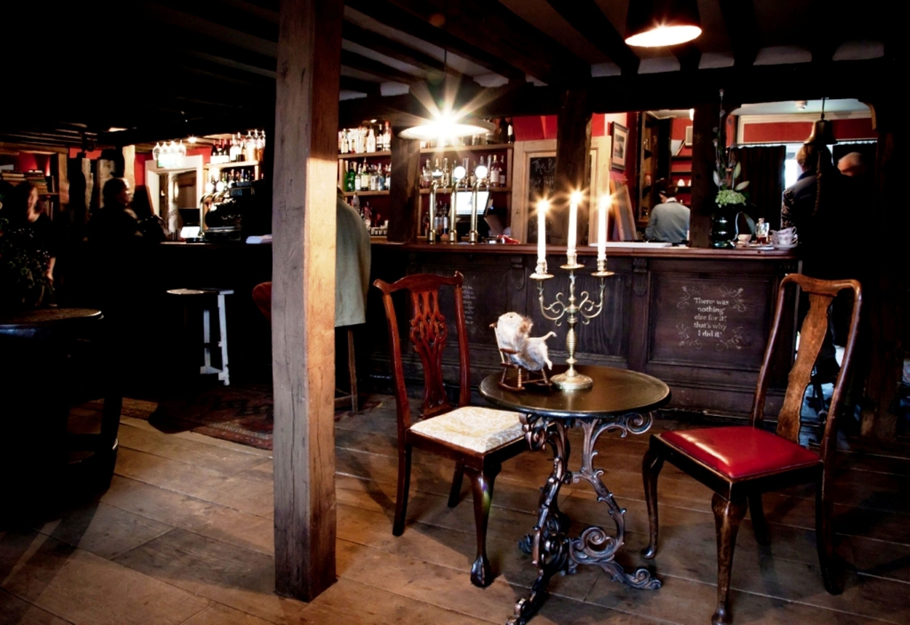 A bar area with wooden chairs, a table with a candelabra, and a bar counter with bottles.