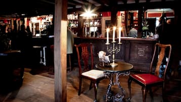 A bar area with wooden chairs, a table with a candelabra, and a bar counter with bottles.