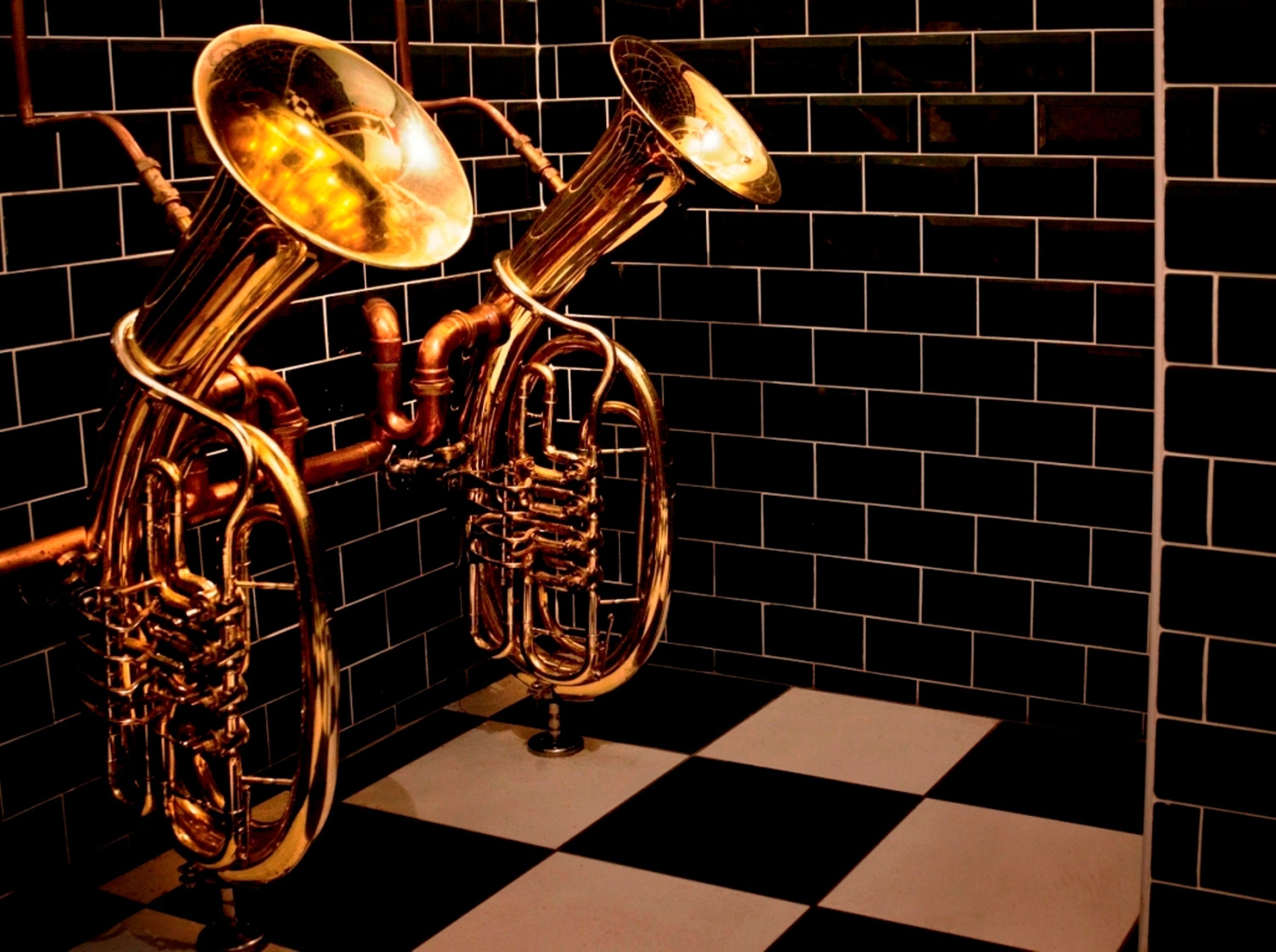 A brass musical instrument, possibly a tuba, against a black and white checkered floor and a black tiled wall.