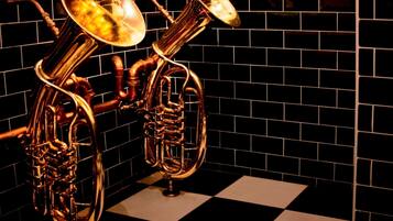 A brass musical instrument, possibly a tuba, against a black and white checkered floor and a black tiled wall.