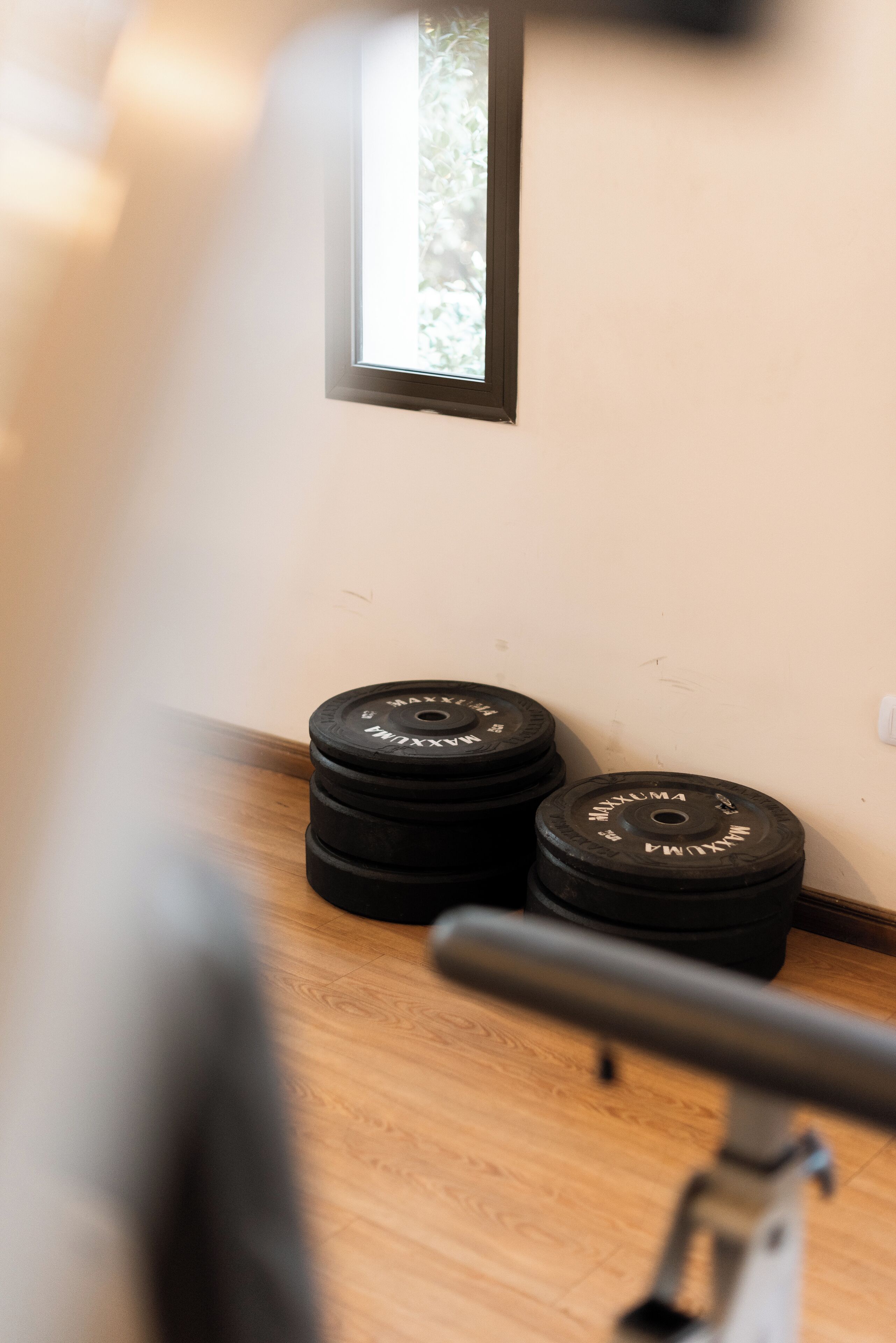 Une salle de sport avec un plancher en bois, une fenêtre et des haltères noirs.