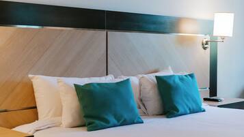 A neatly made bed with white and green pillows, a wooden headboard, and a bedside lamp.