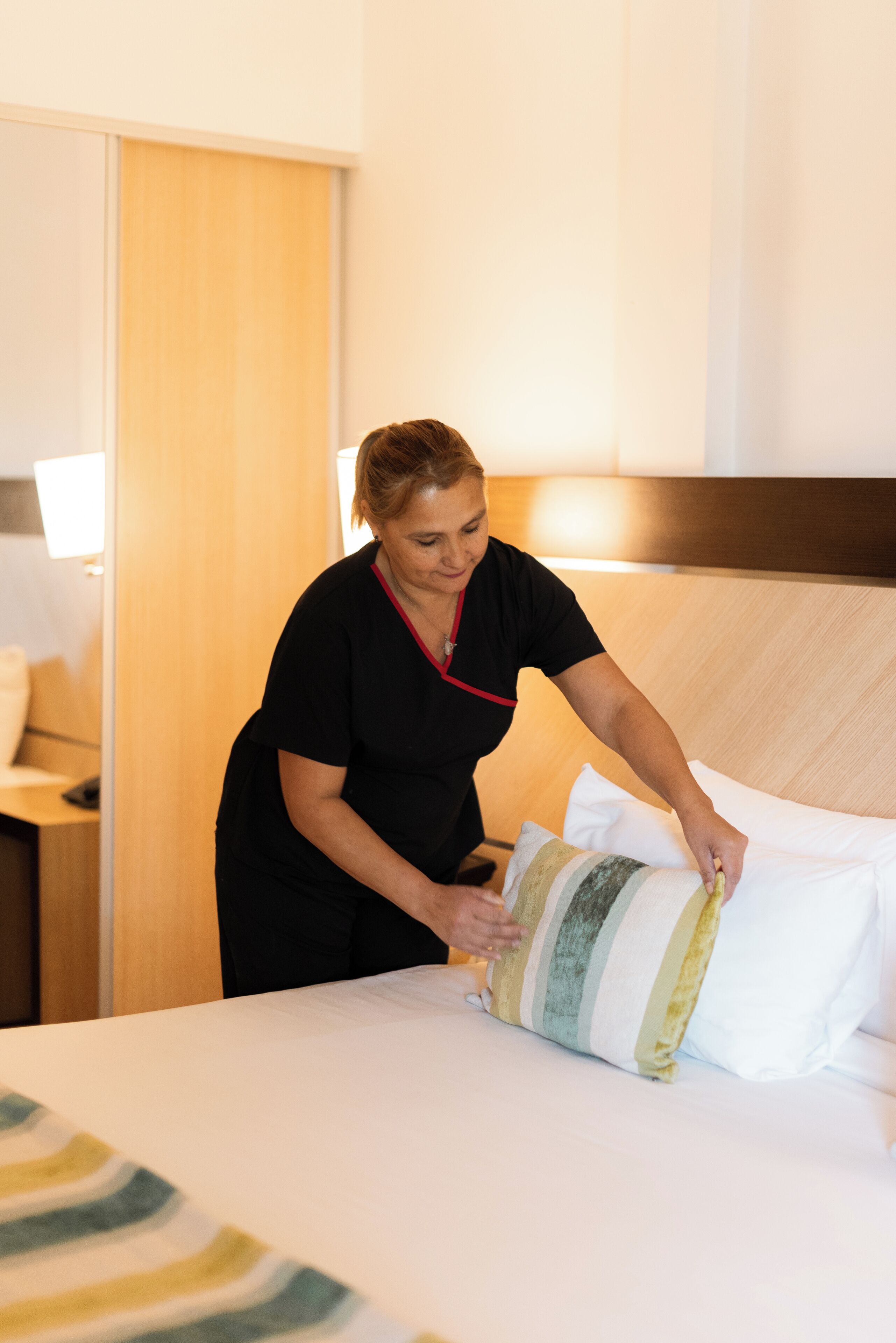 Una persona acomodando almohadas en una cama de habitación de hotel.