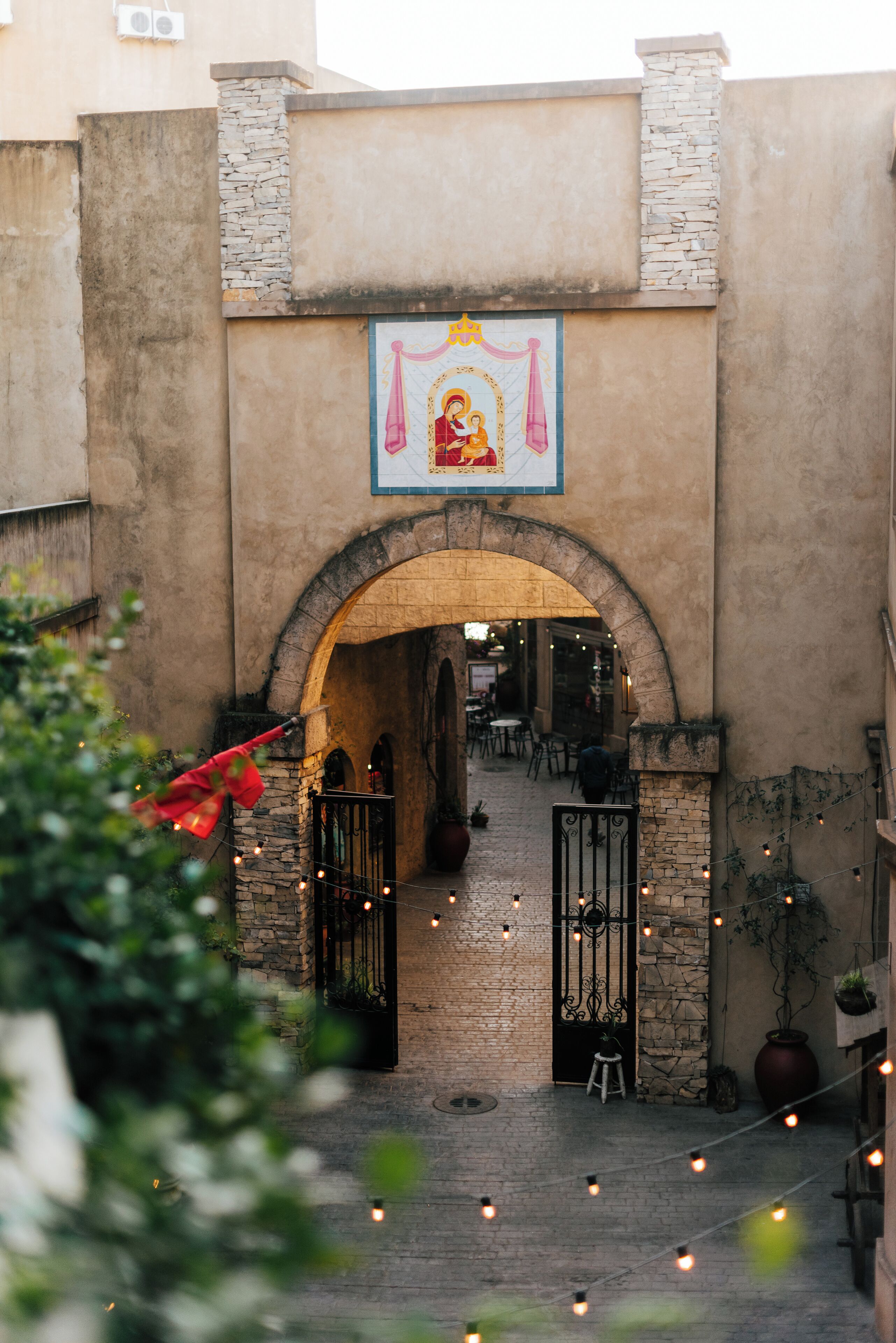 Una entrada en arco con muros de piedra, un letrero colgante y luces de cadena.