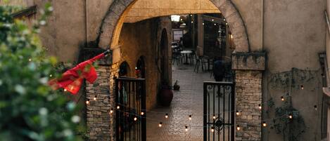 Una entrada en arco con muros de piedra, un letrero colgante y luces de cadena.